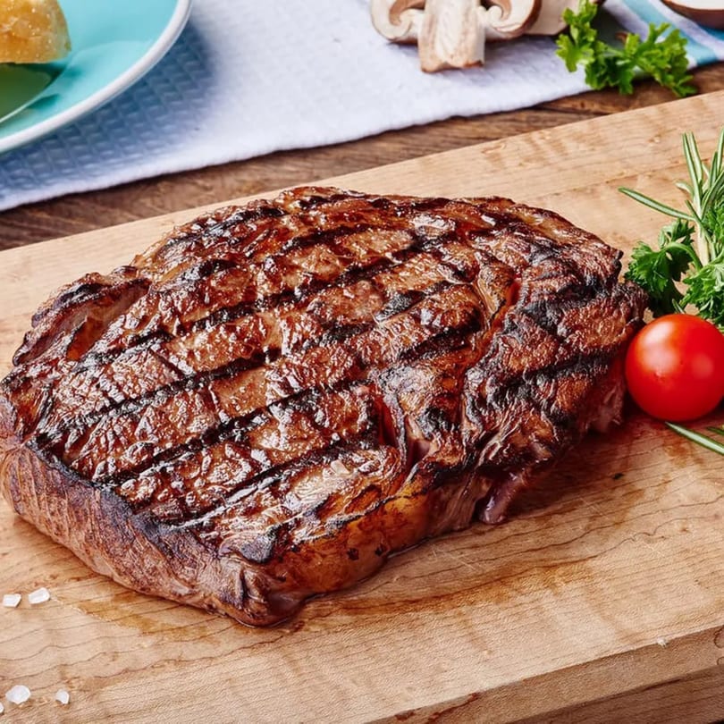 Grilled steak with grill marks, a tomato, and herbs on a wooden cutting board at I Don't Know Diner.